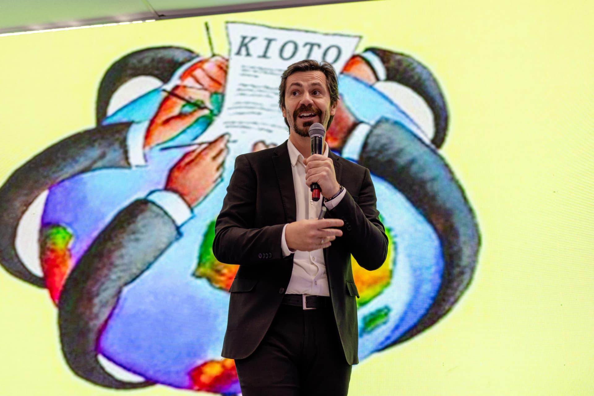 Ricardo Scappini falando de frente com uma ilustração no telão