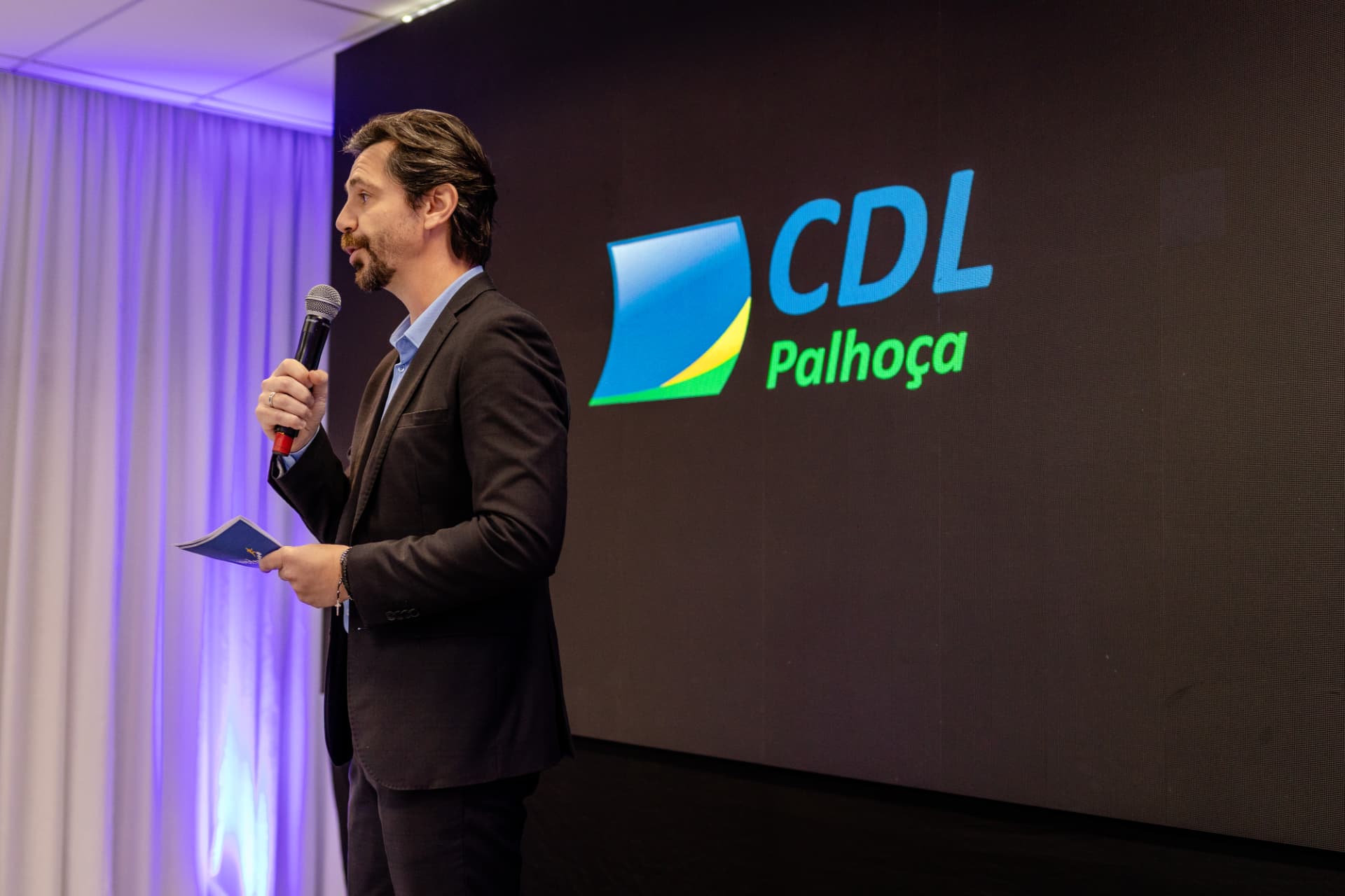 Ricardo Scappini palestrando com a marca CDL Palhoça ao fundo